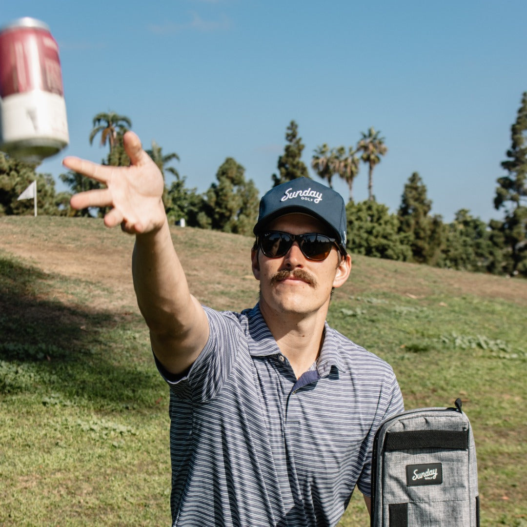 man tossing beverage wearing navy rope hat