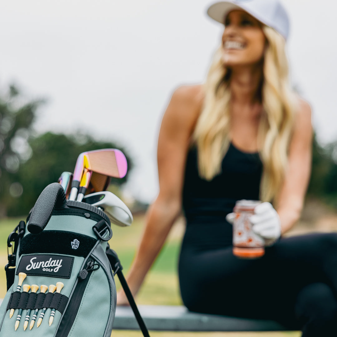 Seafoam Loma Bag by Sunday Golf with Tees, clubs, and woman smiling in background
