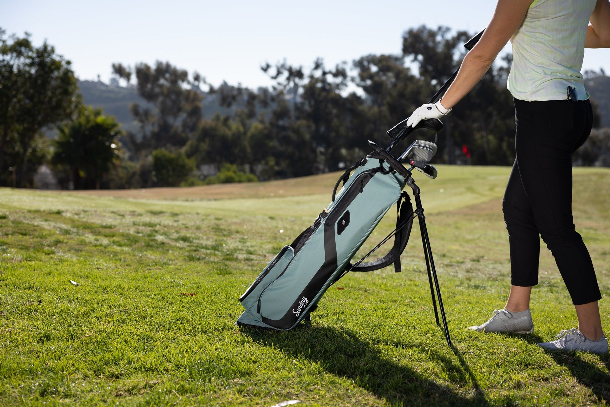 woman putting clubs in the seafoam green El Camino golf bag by Sunday Golf
