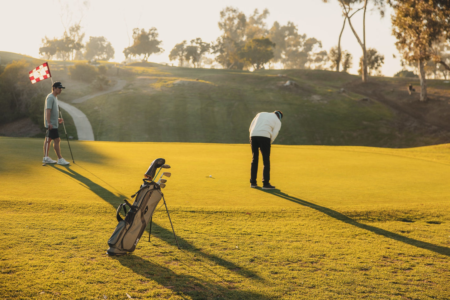 Midnight Green El Camino Golf bag by Sunday Golf on golf course with two golfers on the green putting