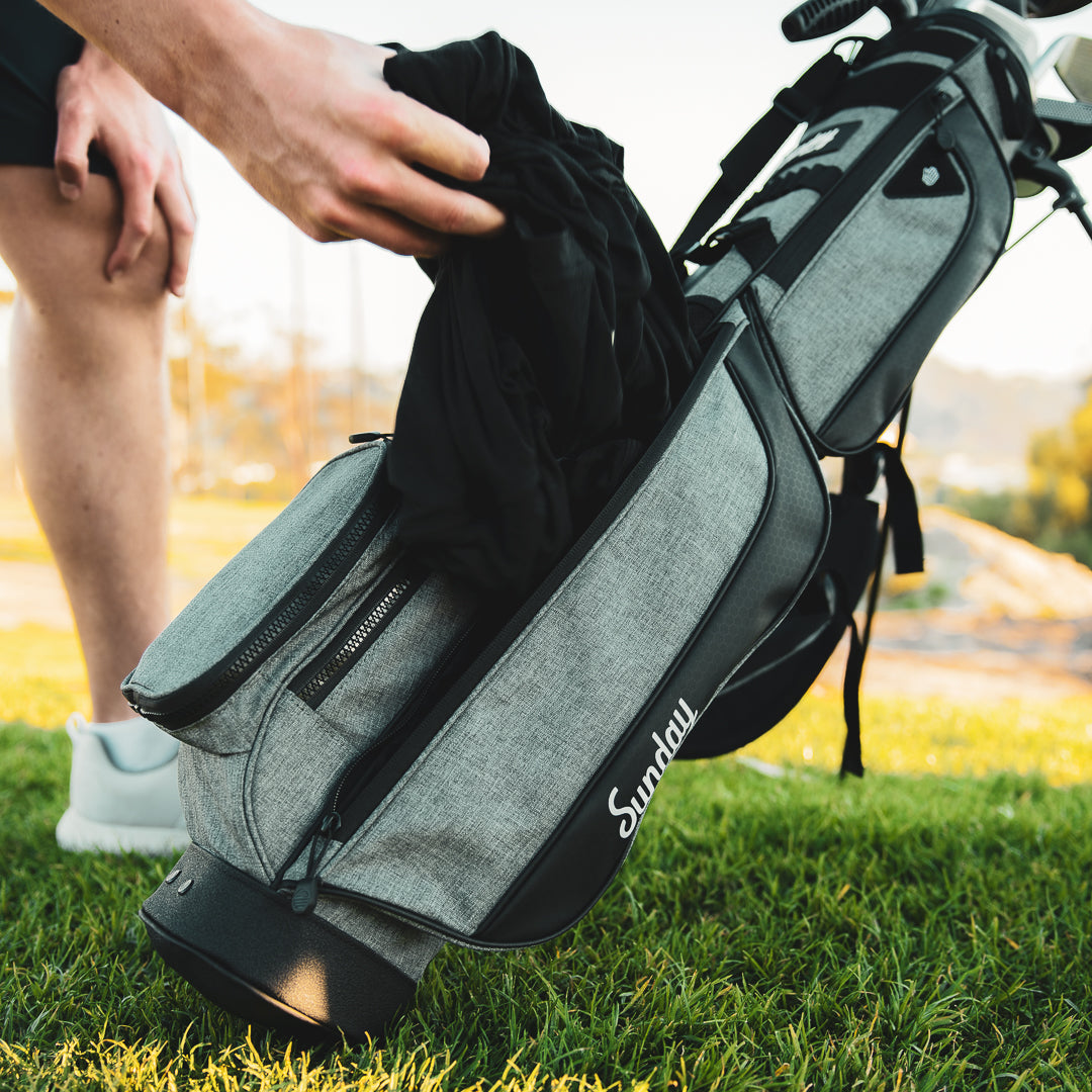 Jacket being pulled out of the storage pouch on the Loma XL Bag by Sunday Golf in Grey