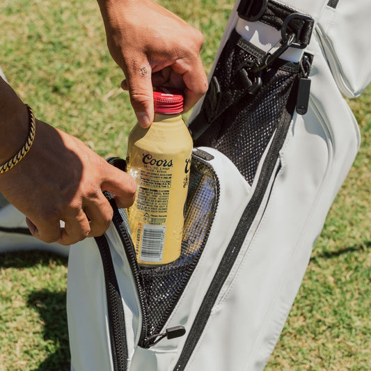 Close-up of golfer placing bottled drink into insulated pocket of white golf bag