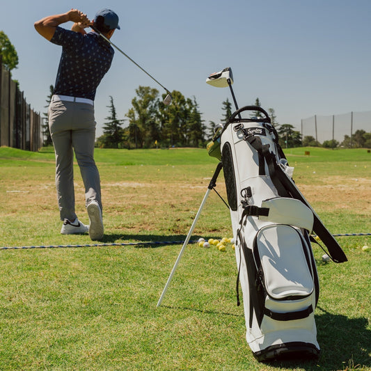 Golfer swinging on driving range with white stand golf bag in foreground