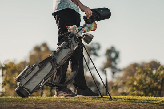 Golfer standing with Sunday Golf stand bag on course with clubs and headcovers