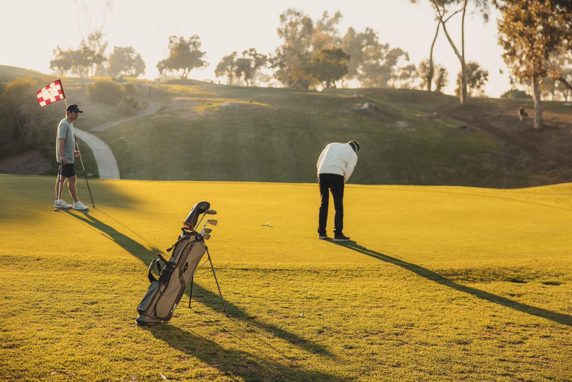 Midnight Green El Camino Golf bag by Sunday Golf on golf course with two golfers on the green putting 